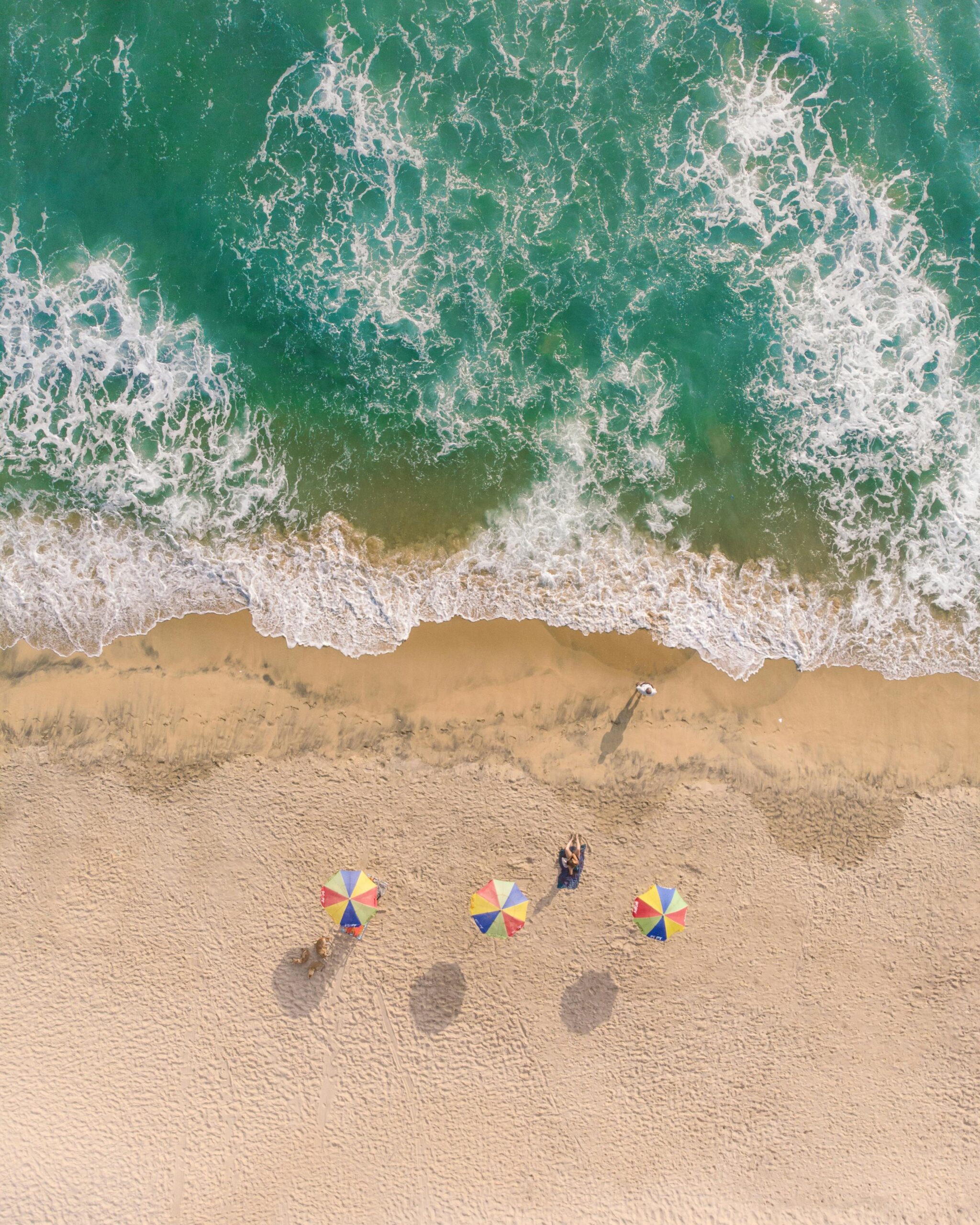 Captivating aerial shot of Varkala Beach in India with colorful umbrellas and turquoise waves.